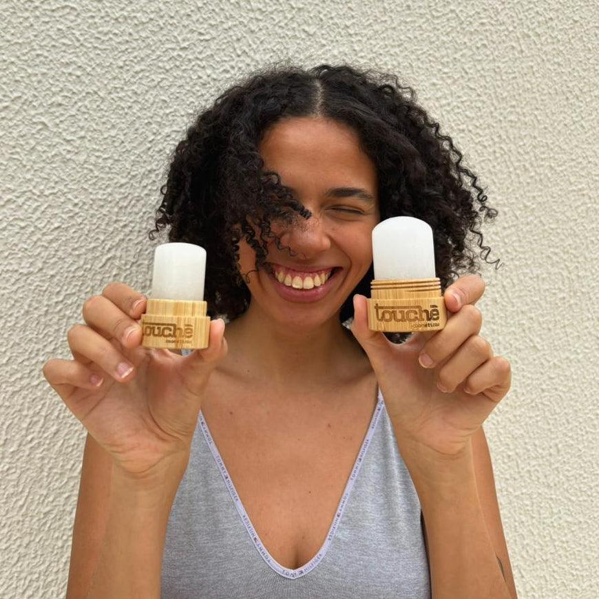 Mulher sorrindo segurando desodorantes de cristal naturais com embalagem de bambu