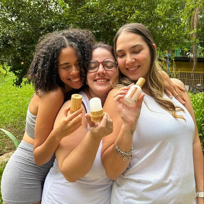 Três mulheres sorrindo ao ar livre com desodorantes naturais