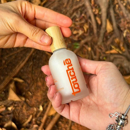 Desodorante spray natural da Touché Cosméticos segurado em mãos ao ar livre